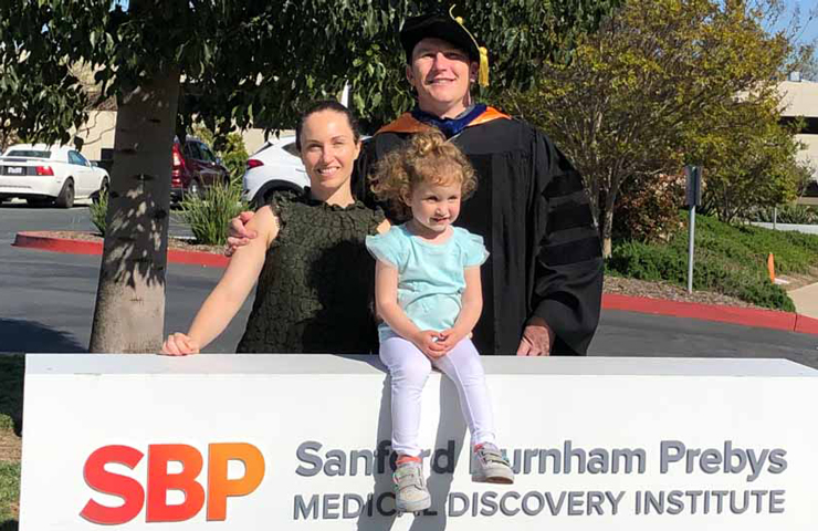 PhD graduate Clyde Campbell with his daughter and wife in front of Sanford Burnham Prebys sign