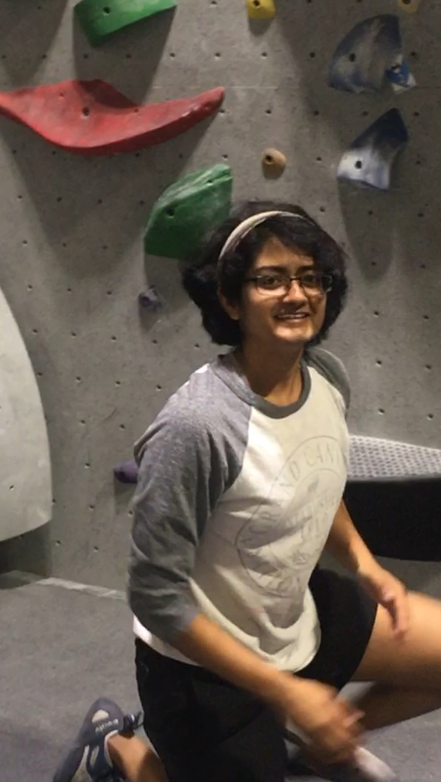 A woman in workout clothes kneeling in front of a rock climbing wall