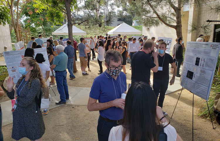 People presenting scientific posters at an outdoor event with tents and trees in the background