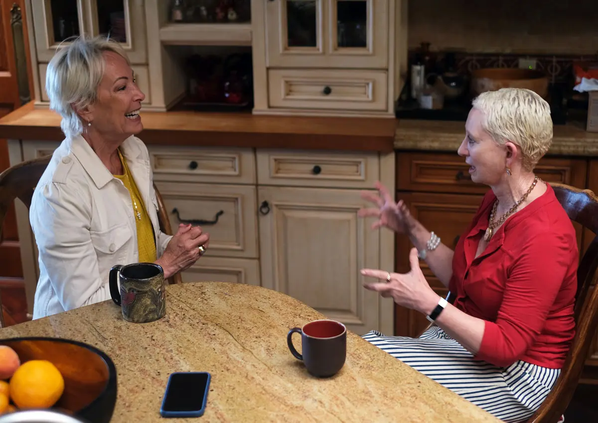 Helen Eckmann and Ruth Claire Black sit and talk at a kitchen table