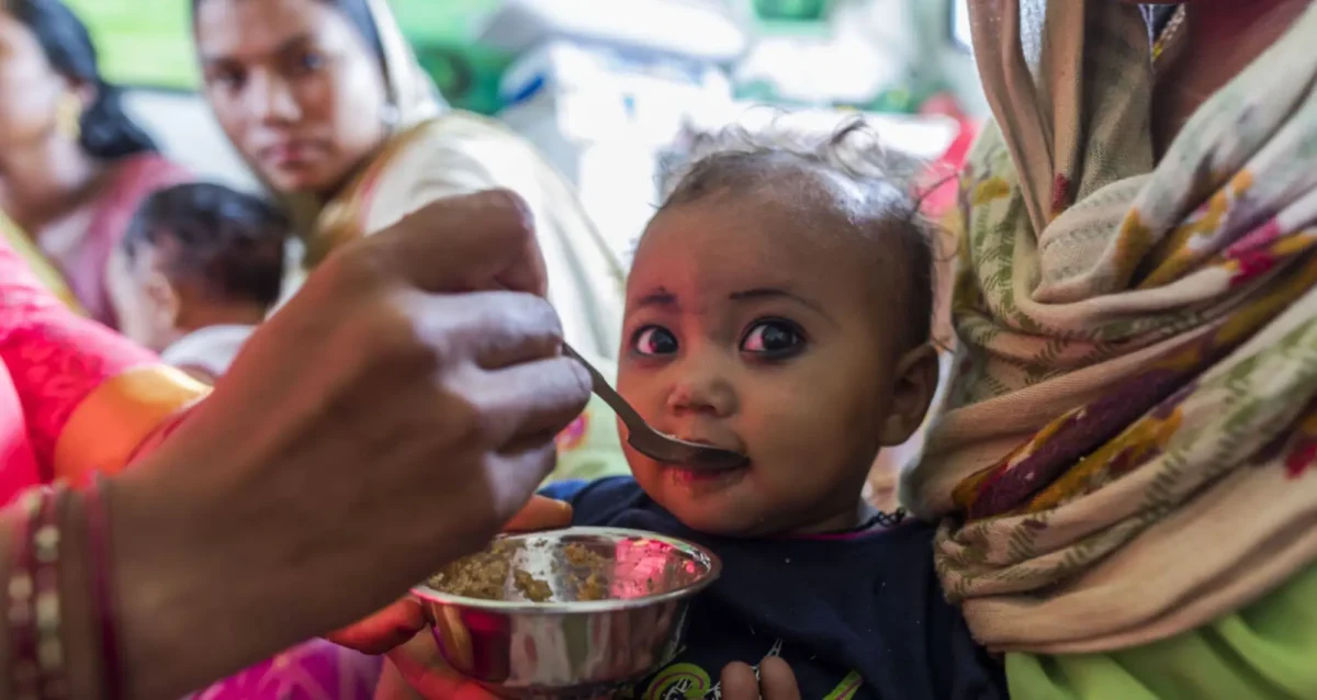 child being spoon fed with family in background