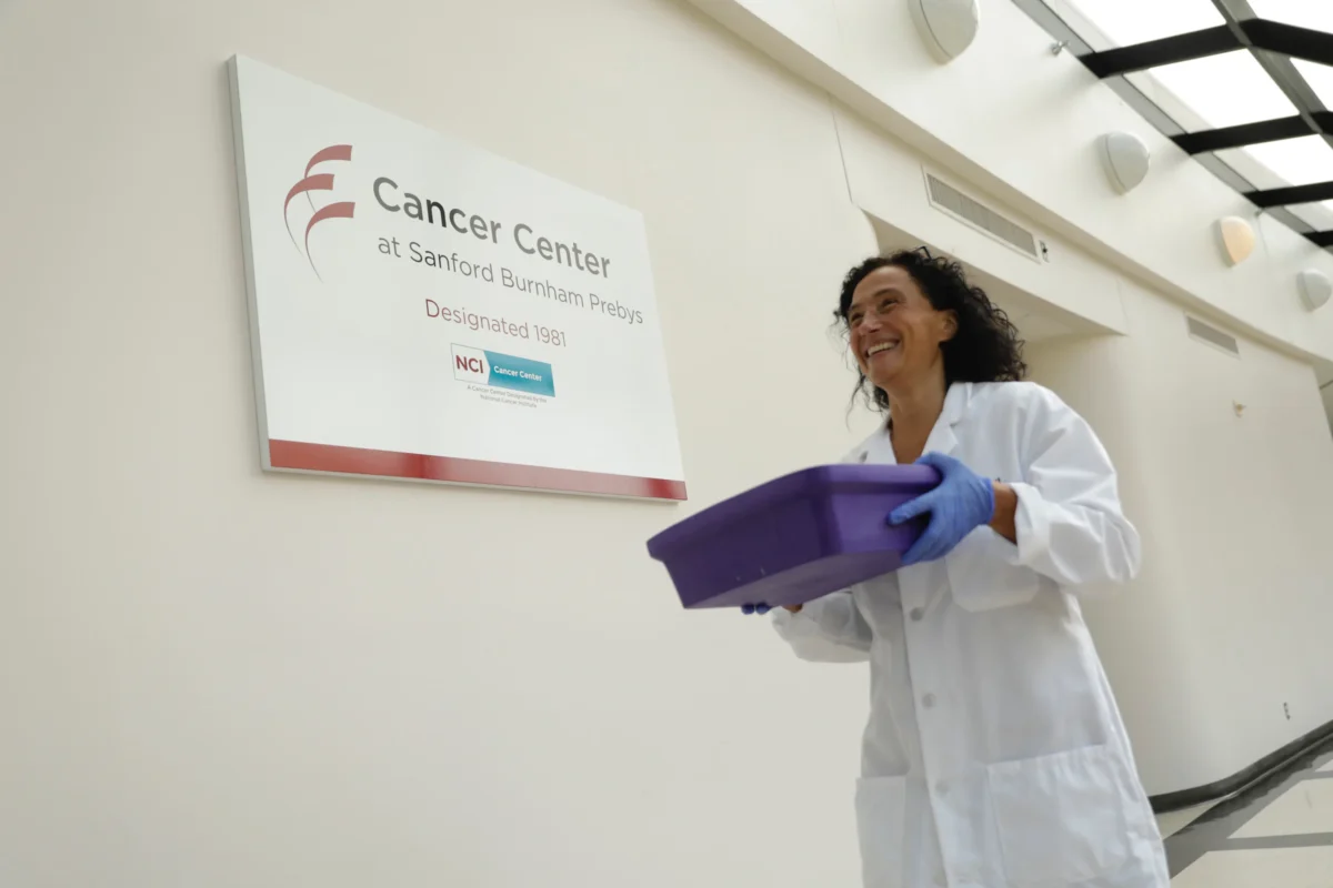 Marzia Scortegagna in lab coat walking past Cancer Center sign holding tray