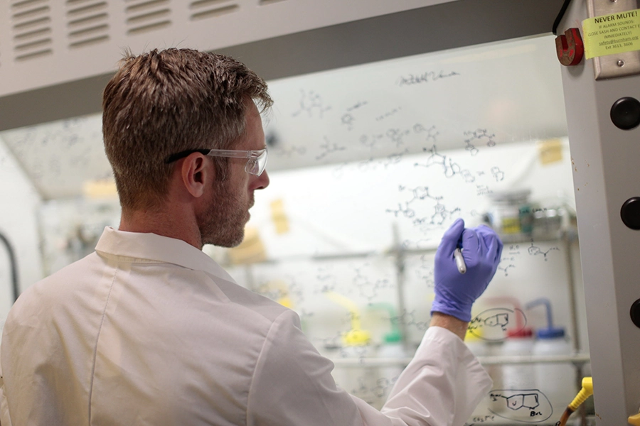 A scientist draws chemical structural diagrams on a fume hood that captures and removes vapors to ensure safety during experiments conducted at Sanford Burnham Prebys.